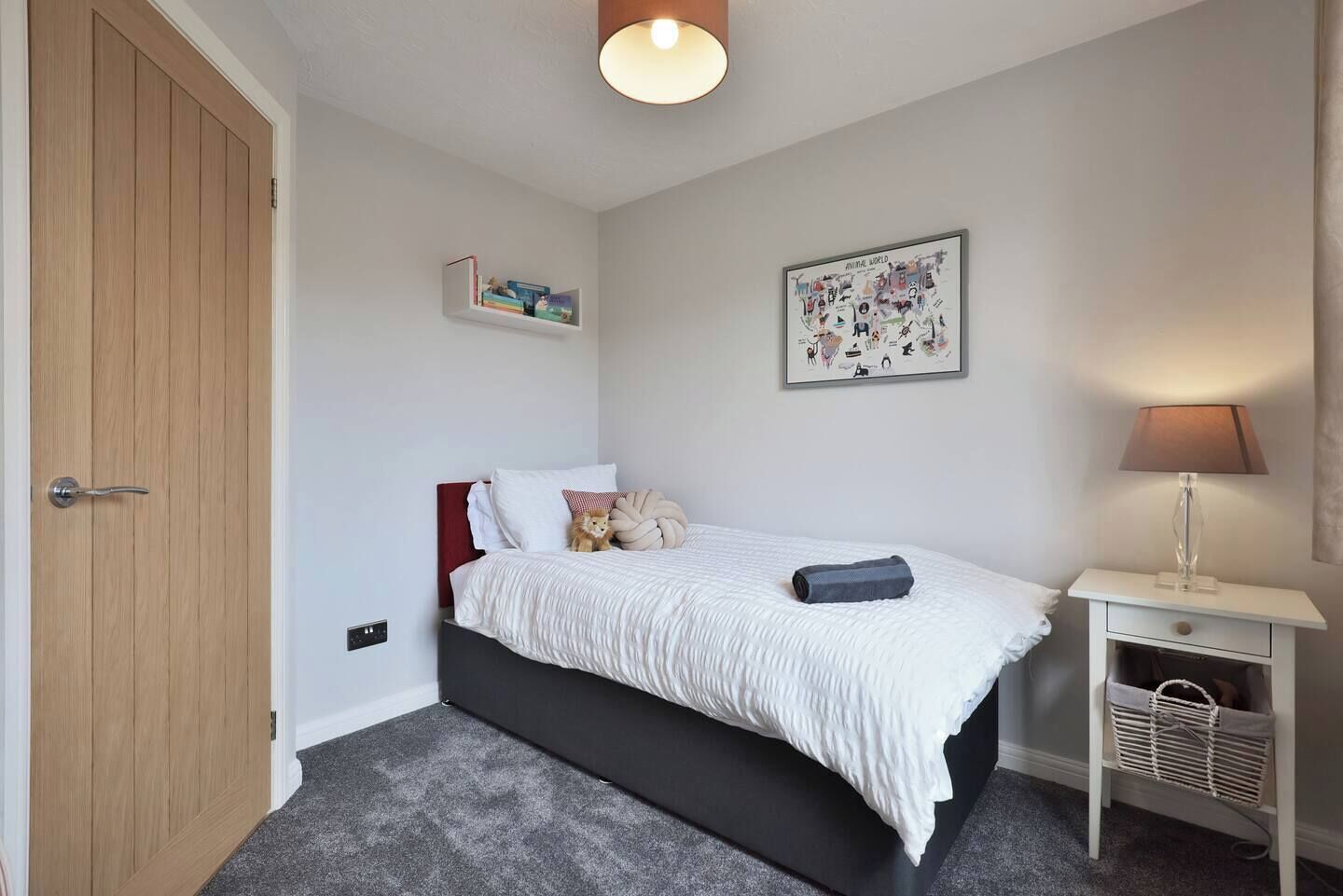 Une chambre à coucher avec un lit, une table de chevet, une lampe, une étagère murale et une porte.