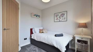 Une chambre à coucher avec un lit, une table de chevet, une lampe, une étagère murale et une porte.