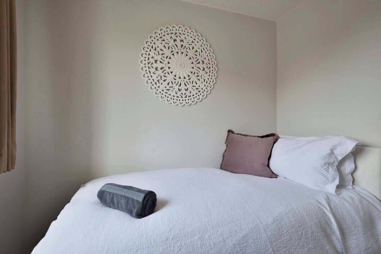 A neatly made bed with a rolled towel, a decorative wall piece, and two pillows.