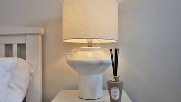Een nachtkastje met een witte lamp, een geribbelde lampenkap en een decoratieve vaas met zwarte takken.