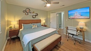 A bedroom with a bed, bedside tables, a ceiling fan, a TV, and a desk with a chair. - Modern Hickory Hideaway (Hickory)