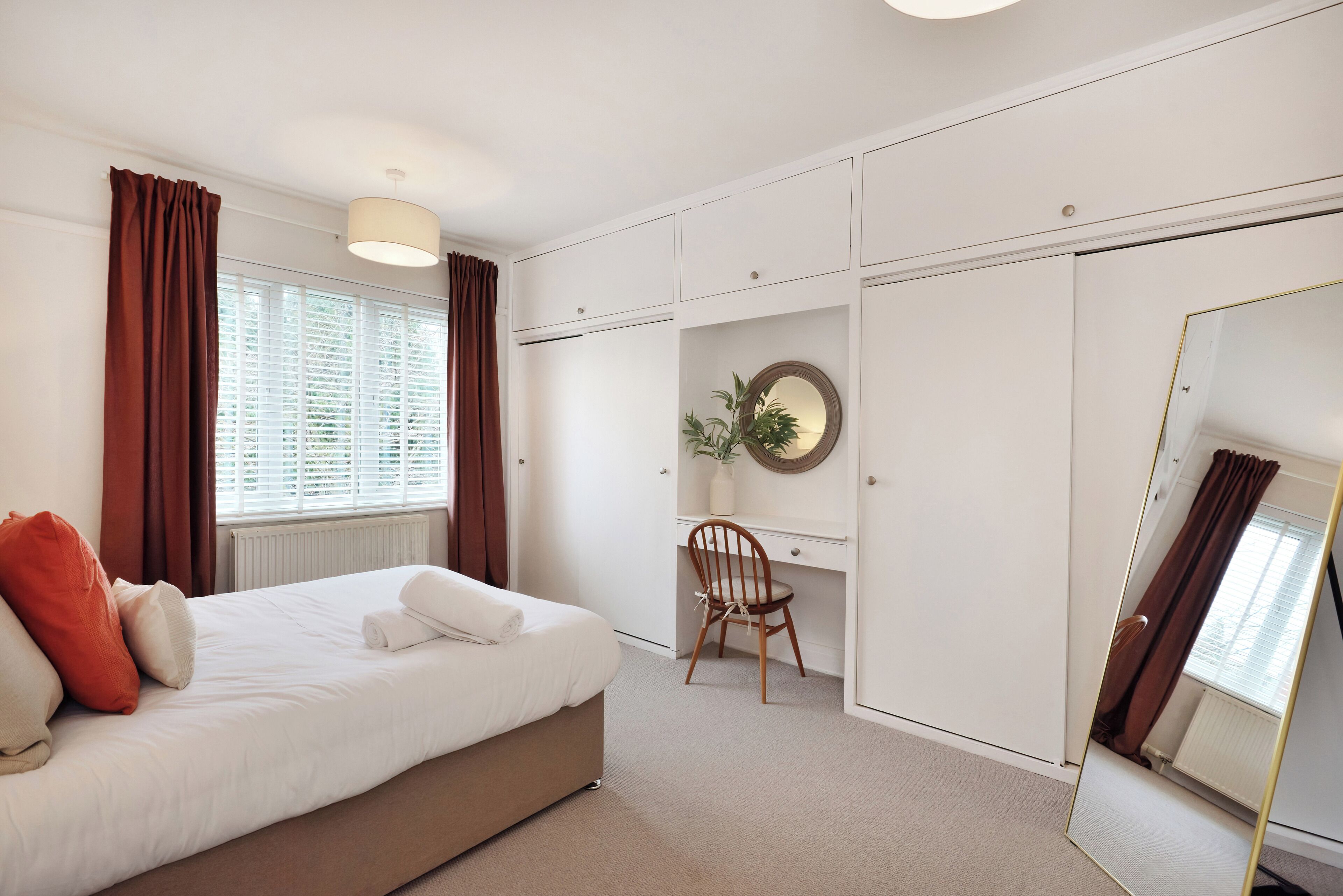 A bedroom with a bed, a desk, a chair, a mirror, and a radiator.