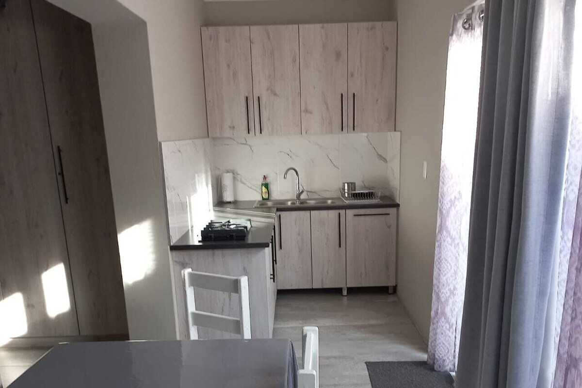 A modern kitchen with light wood cabinets, a marble countertop, and a dining area with a table and chairs.