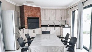 A modern kitchen with a brick accent wall, a built-in oven, and a large dining table with chairs. - Diaz Guesthouse (Mossel Bay)