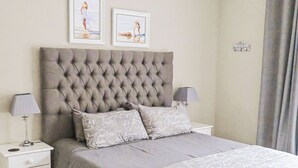 A neatly arranged bedroom with a tufted headboard, a patterned bedspread, and a decorative rug. - Diaz Guesthouse (Mossel Bay)