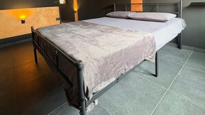Ett modernt sovrum med en stor säng, ett träpanelat tak och en väggmonterad lampa.