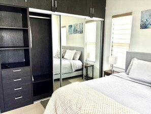 A bedroom with a bed, a wardrobe, a bedside table, and a window with blinds.