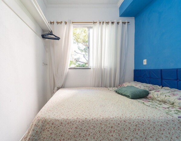 Un dormitorio con cama, ventana con cortinas y pared azul.