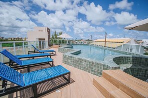 A rooftop pool area with blue lounge chairs, a small pool, and a glass balustrade. - Flat com Wifi a 400m da Praia de Porto de Galinhas (Ipojuca)