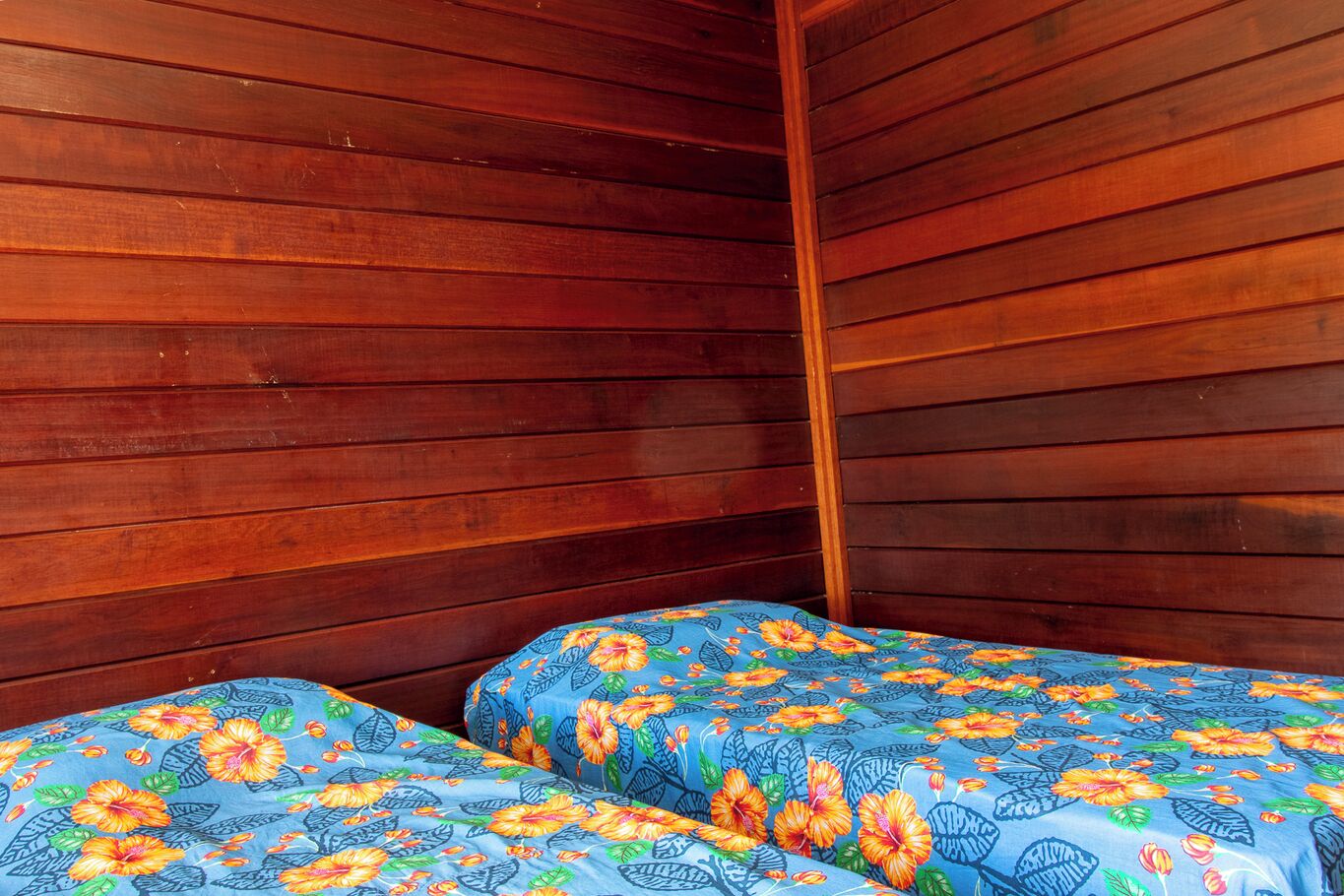 Ein Zimmer mit Holzwänden und zwei Betten mit blumigem Bettzeug.