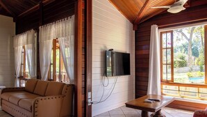 Ein gemütliches Zimmer mit einer Couch, einem an der Wand befestigten Fernseher und einem Tisch mit Blick ins Freie.
