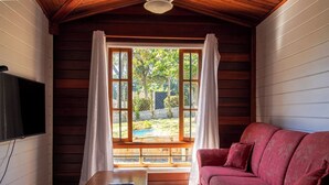 Ein gemütliches Zimmer mit Holzvertäfelung, einem roten Sofa, einem Fernseher und einem Fenster mit Vorhängen.