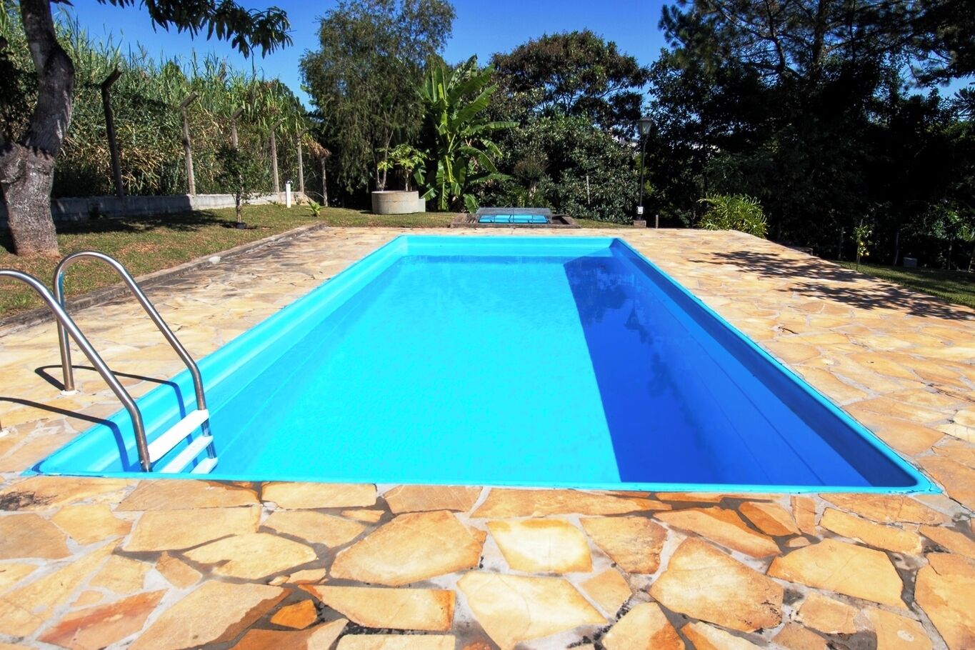 A rectangular swimming pool with a stone deck, metal ladder, and a clear blue water surface.