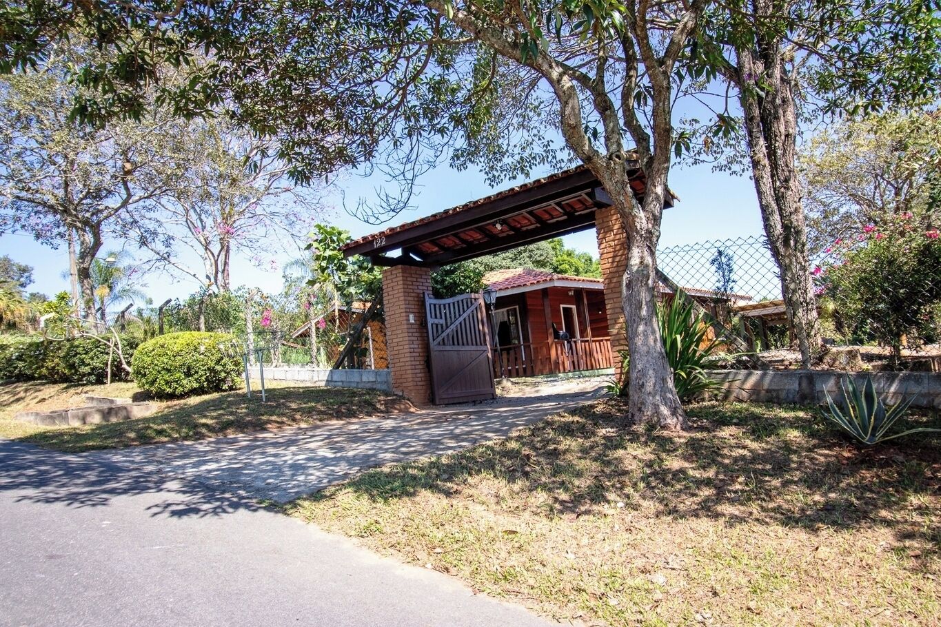 A gated entrance with a covered porch, a brick building, and a fenced area with trees and shrubs.