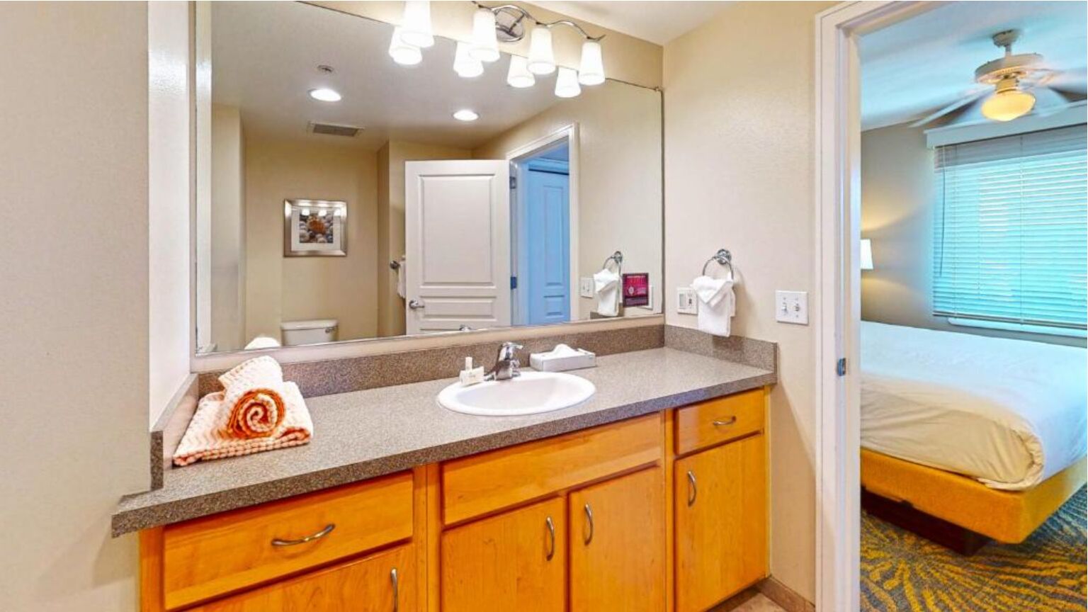 A hotel bathroom with a sink, mirror, and wooden cabinets.
