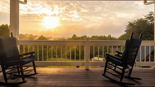 Eine Holzdielen-Terrasse mit zwei Schaukelstühlen, die auf eine Sonnenuntergangsansicht ausgerichtet sind.