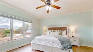 Ein Schlafzimmer mit einem großen Bett, einem Deckenventilator, einem Nachttisch mit Lampe und einem Fenster mit Blick ins Freie.