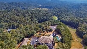 Luftaufnahme eines Hotels, umgeben von dichtem Wald, mit sichtbarem Schwimmbad und Parkplatz.