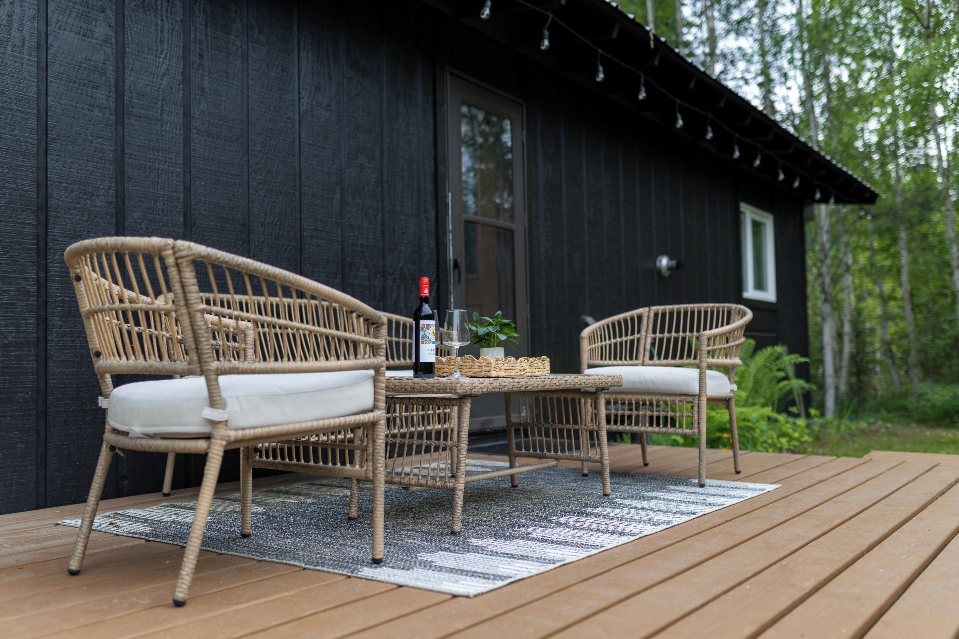 A wicker outdoor seating area with a bottle and glass, near a dark wooden building.