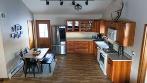 A compact kitchen with wooden cabinets, a refrigerator, a stove, and a dining area with a table and chairs.