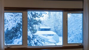 A room with a large window overlooking a snow-covered landscape, including a cabin and trees.