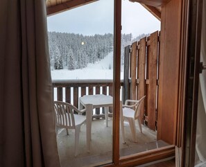 Un balcón de madera con una mesa y sillas, con vistas a un bosque nevado.