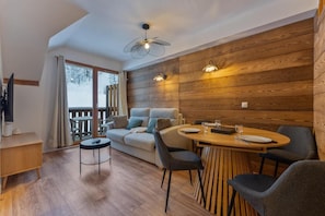 Una habitación acogedora con sofá, una mesa de comedor con sillas, televisor y pared de madera.