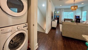 A laundry room with stacked washers and dryers, a hallway leading to a living area with a sofa and a foosball table, and a staircase.