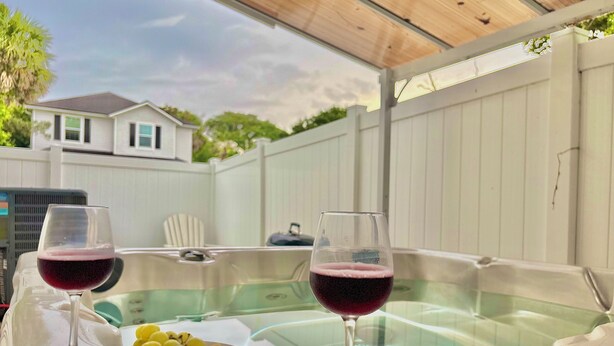 A hot tub with two glasses of red wine and a plate of fruit.