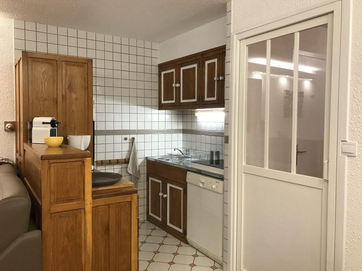 A compact kitchen with wooden cabinets, a dishwasher, and a tiled backsplash.