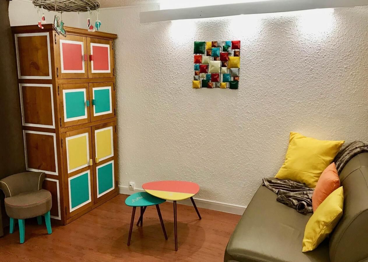 Ein Zimmer mit einem Holzkasten, einem kleinen Tisch, einer Couch und einem farbenfrohen Wandbild.