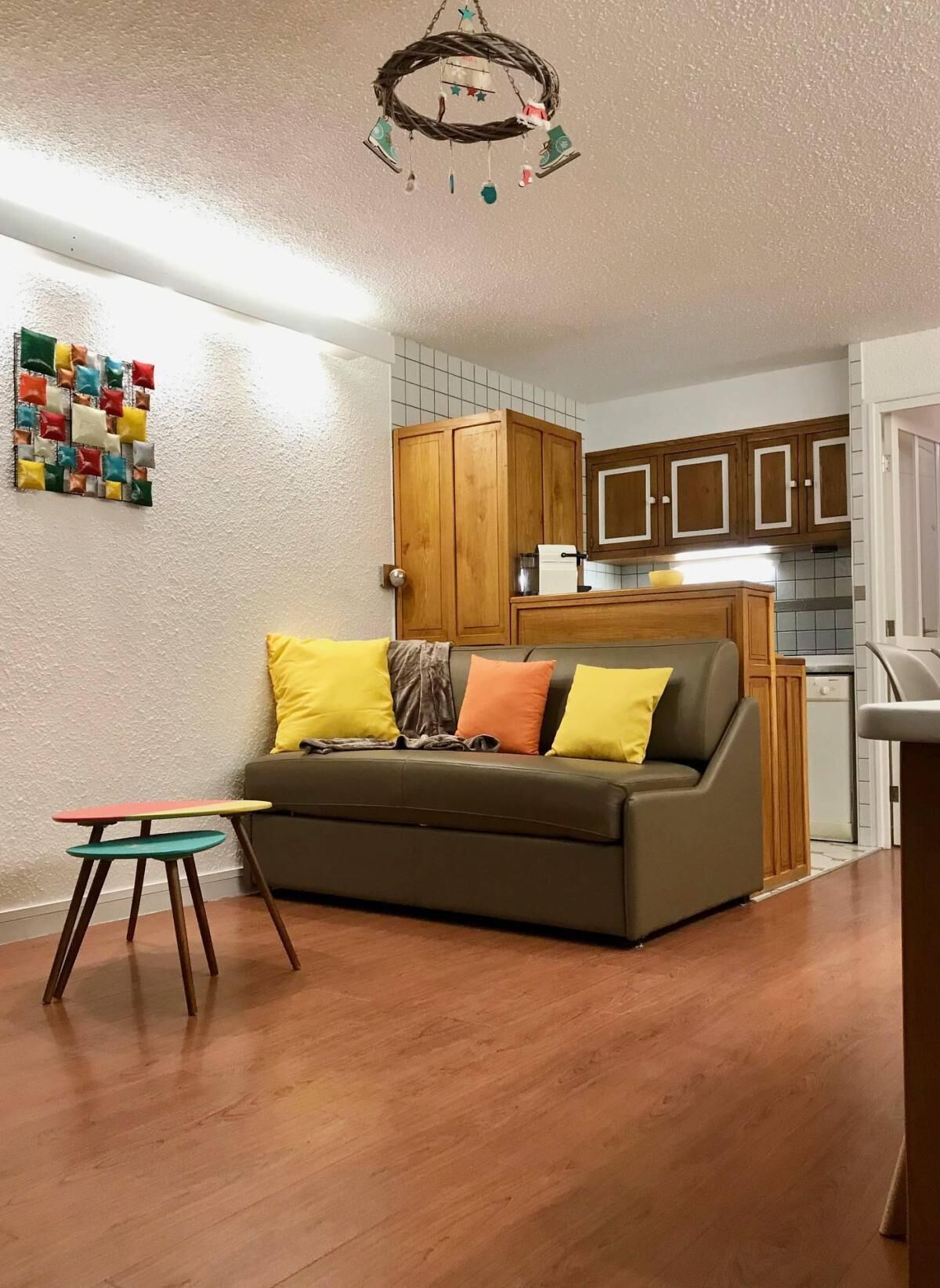 A cozy living room with a sofa, a small table, and a kitchen area in the background.