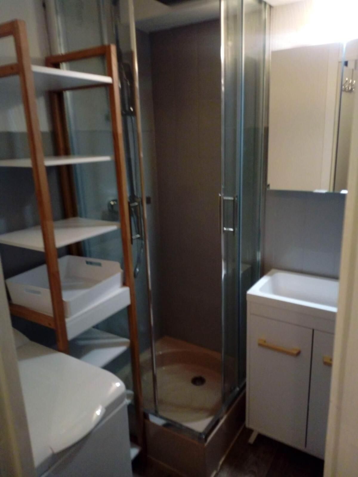 A small bathroom with a glass shower enclosure, a wooden ladder, and a white sink.