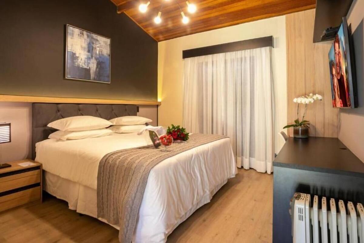 A modern bedroom with a large bed, wooden ceiling, and a bedside table with a vase of flowers.