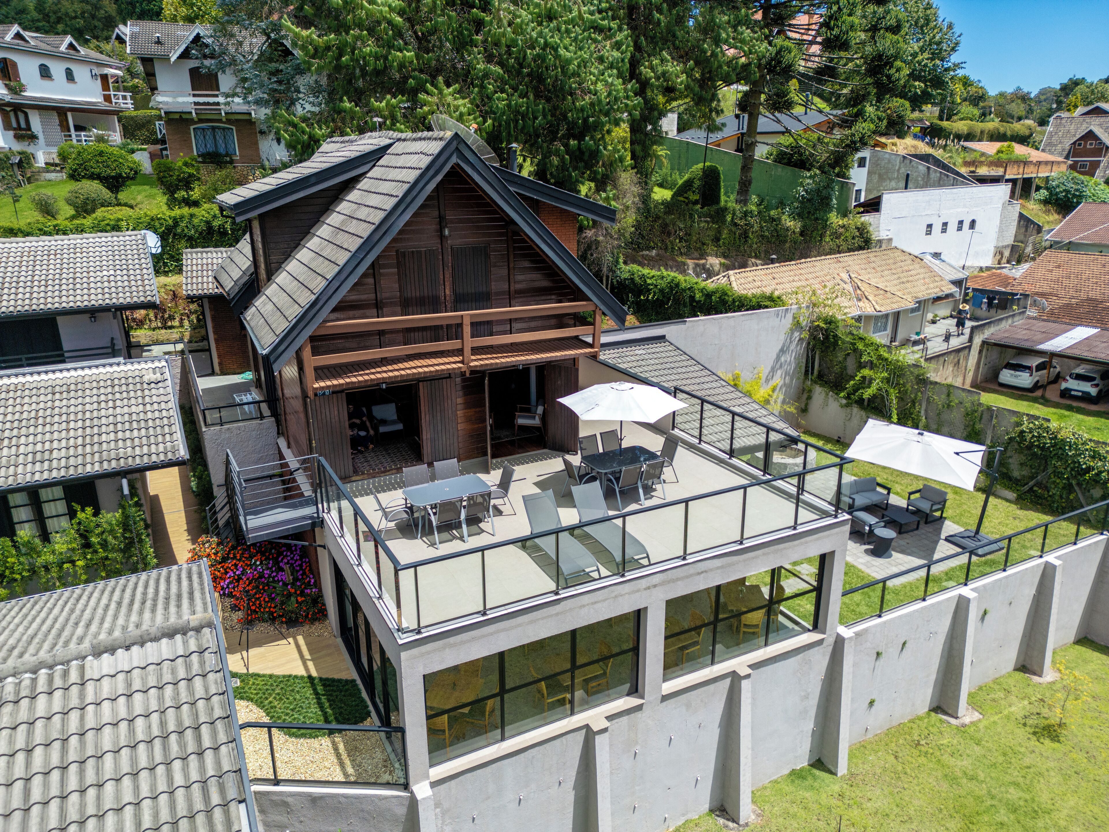 Une maison moderne dotée d’un grand balcon en verre, d’une terrasse en bois et d’un petit jardin.