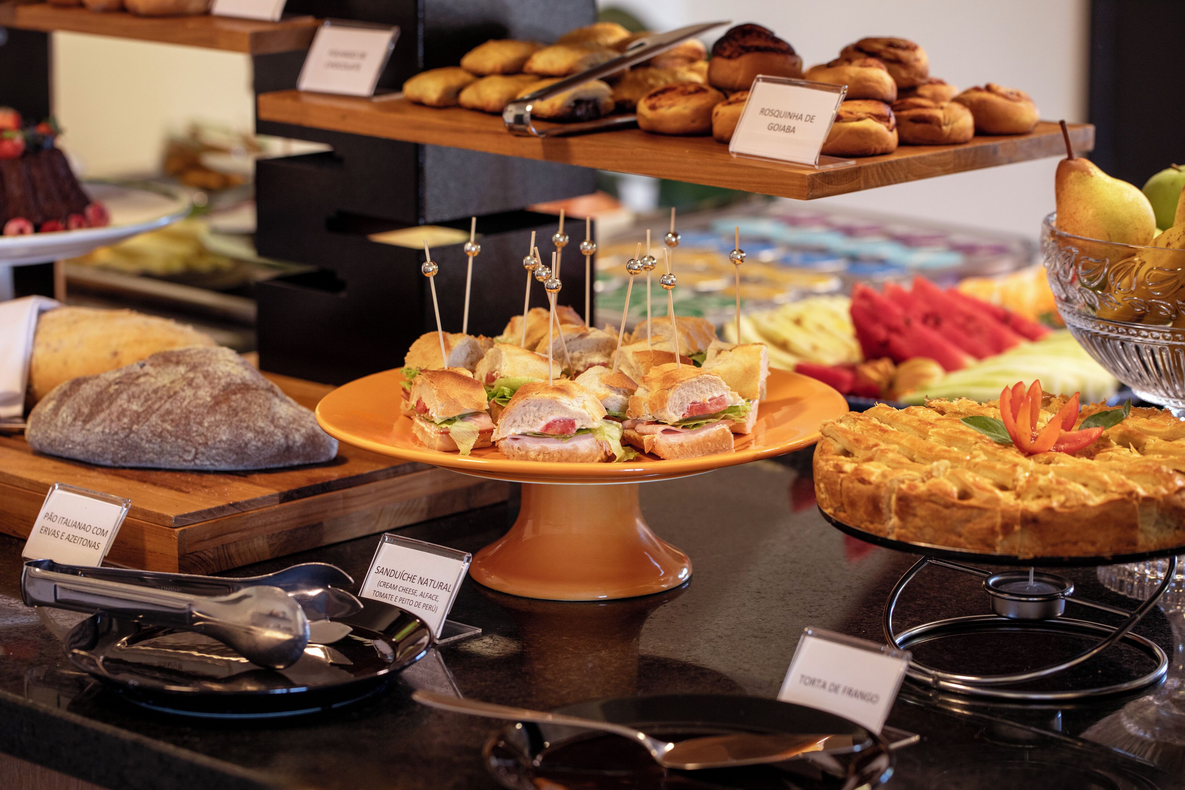 A buffet with various food items including sandwiches, pastries, and a fruit bowl.