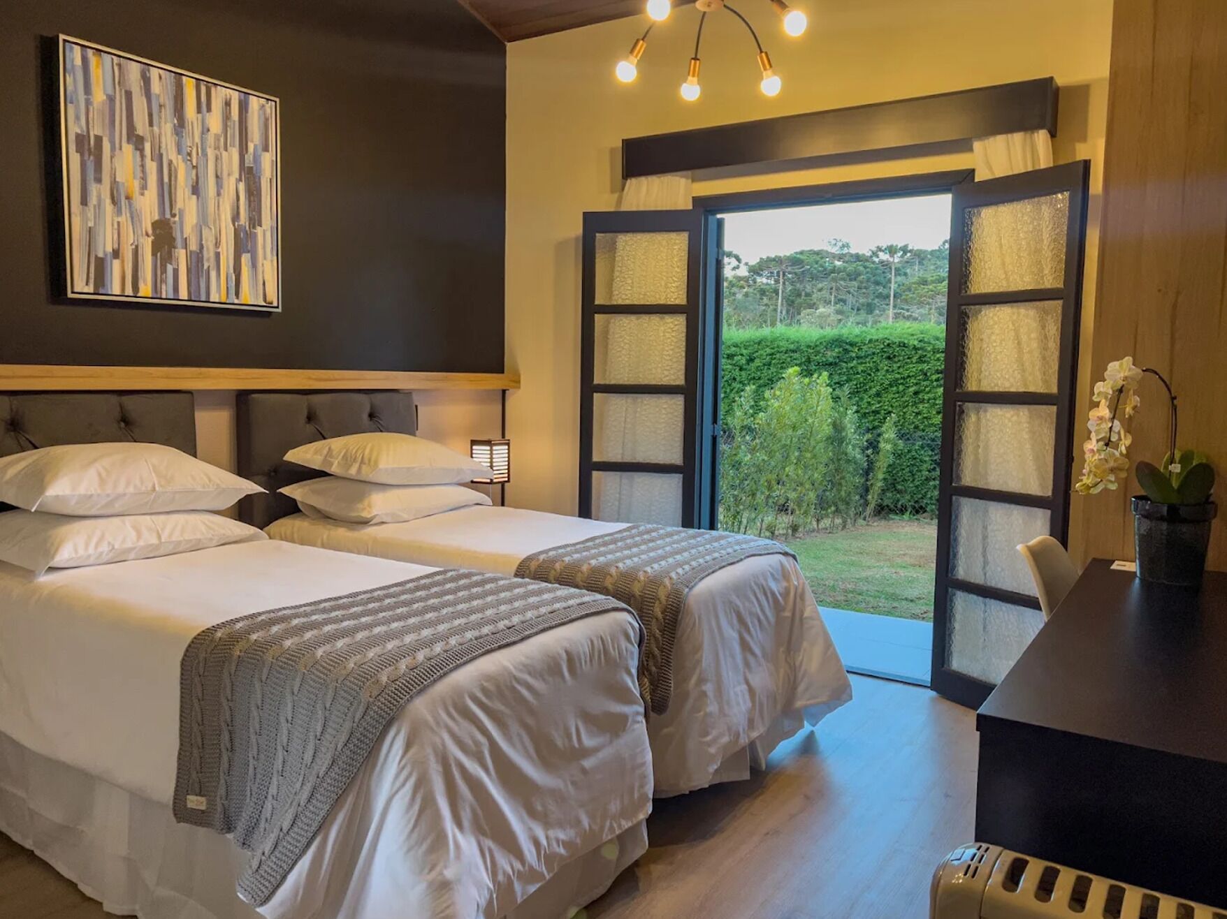 A hotel room with two beds, a desk, and a view of the outdoors.