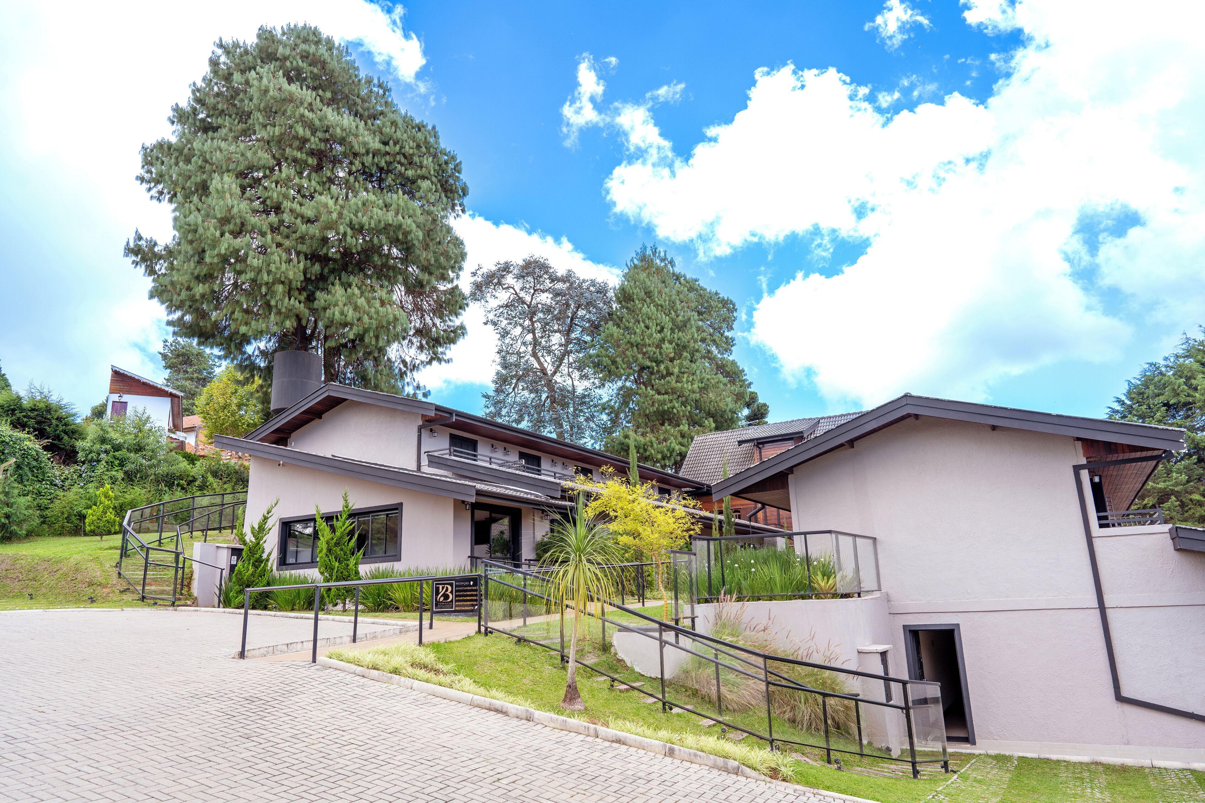 A modern two-story house with a paved driveway, a staircase, and a large tree in the front yard.