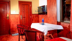 A hotel room with a wooden door, a television mounted on the wall, a table with a white tablecloth, and a red sofa.