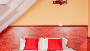 A hotel room with a wooden headboard, a bed with red and white bedding, a small table, and a wall-mounted lamp.
