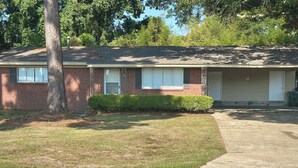 A two-story brick building with a garage, a well-maintained lawn, and a tree in front. - 3BR Midtown Stay! Located on USM Campus!!  Perfect for Game Days and Getaways (Hattiesburg)