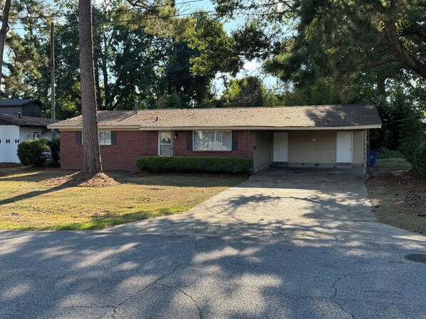 A single-story brick house with a front garage door, a small front yard, and a driveway leading to the garage.