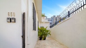 A narrow alleyway with a white wall on the left, a black metal gate, and a number '650' above a door. - Luz Collection 3bedroom San Juan (San Juan)