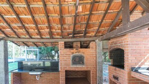 An outdoor kitchen with a brick oven, a sink, and a pergola structure. - Cavalinho Branco Flat Para 4 Pessoas c Piscina (Águas de Lindóia)