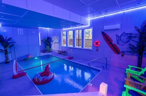 Una piscina interior con un tiburón inflable rojo, una plataforma de salto y un flotador en la pared.