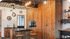 A modern kitchen with wooden accents, a central island with stools, and a visible microwave. - Le Chai des Tortues · Character home · Beach 250 m (Rivedoux-Plage)