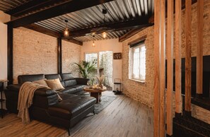 A cozy living room with a black leather sofa, a round wooden coffee table, and a stone wall. - Le Chai des Tortues · Character home · Beach 250 m (Rivedoux-Plage)
