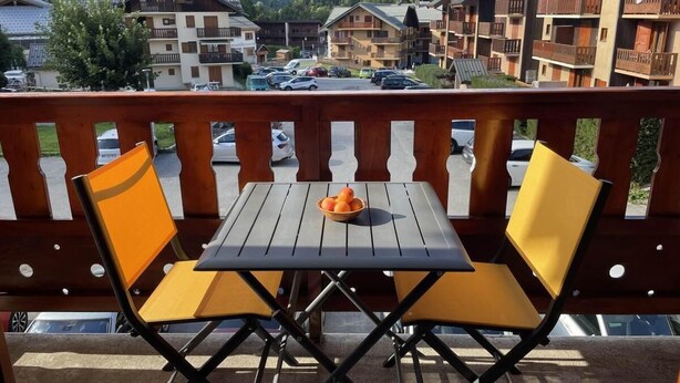 A balcony with two yellow chairs and a table, overlooking a parking area and buildings with wooden balconies. - 230m from ski slopes, 1st floor, balcony, tv, ski locker, 32m², Valloire (Valloire)