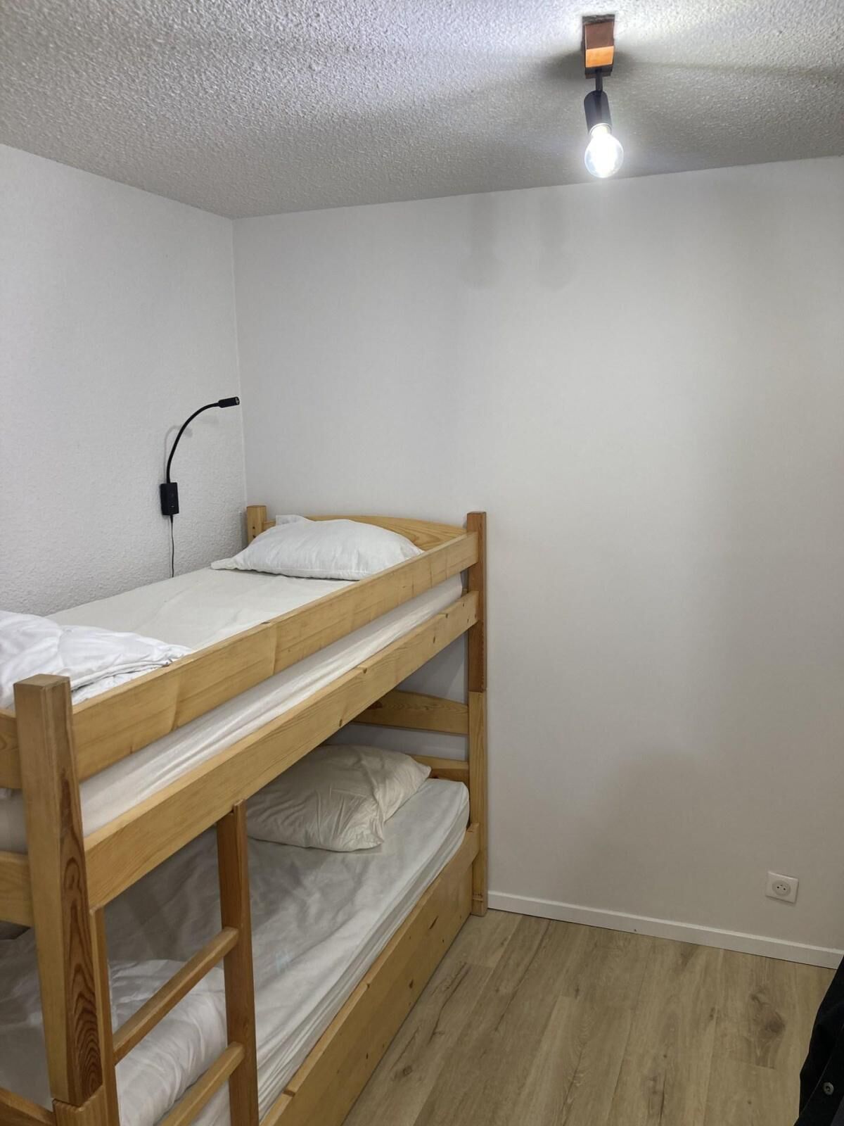 A bunk bed room with a white ceiling, a single light fixture, and a power outlet on the wall.
