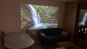 A living room with a wooden table, a dark-colored sofa, and a large window displaying a waterfall scene. - 230m from ski slopes, 1st floor, balcony, tv, ski locker, 32m², Valloire (Valloire)